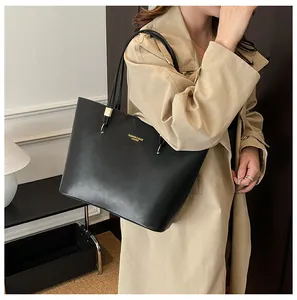 Detailed view of black patent leather tote bag styled with khaki trench coat for workwear