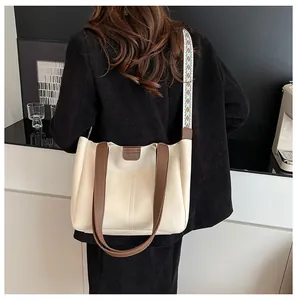 Detail of a large cream tote bag with brown trim and patterned blue strap worn by model
