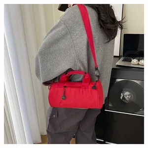 Red cylindrical travel duffel bag with wide straps shown in a modern lifestyle setting