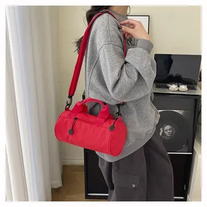 Detail of red cylindrical duffel bag with handles and adjustable shoulder strap on a desk
