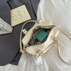 Elegante cremefarbene Boston-Handtasche mit Plüschbommel und Alltagsgegenständen darin