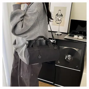 Side view of a model wearing a black cylindrical nylon travel bag with adjustable shoulder strap