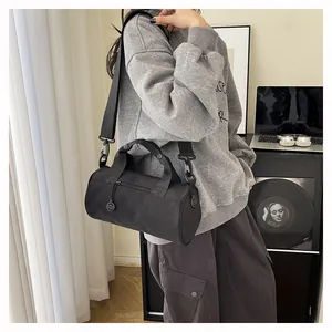 Close-up of a black nylon cylinder sports bag worn crossbody by a model in a casual setting