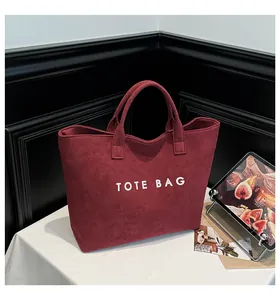 Detail of burgundy suede tote bag featuring white embroidered TOTE BAG text on surface