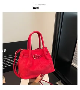 Detail of red faux suede handbag showing matte texture and gold buckle accents