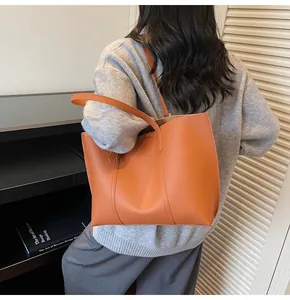 Dettaglio di una borsa tote in pelle opaca arancione con spalline sottili indossata