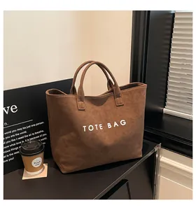 Detailed view of a brown suede tote bag with bold white TOTE BAG text on a desk