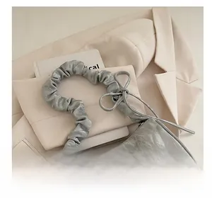 Macro view of pleated grey shoulder bag fabric with small silver bow detail and strap