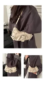 Detail einer cremeweißen Halbmond-Schultertasche mit Schnallen und Punk-Nieten