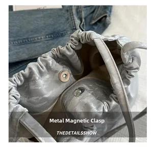 Detail of magnetic snap closure on a grey pleated cloud bag with marble texture finish