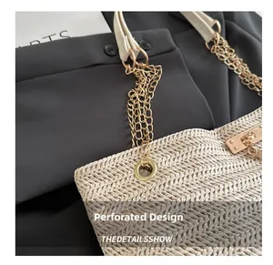 Dettaglio della borsa in paglia beige con design a occhielli e catena dorata