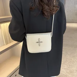 Détail du sac bandoulière en cuir crème texturé avec logo en croix argentée