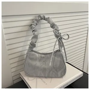 Detail of silver pleated handbag with metal bow accent and marble texture on white books