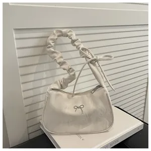 Detail of creamy white ruched underarm bag featuring marble texture and silver bow charm