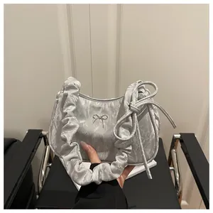Detail of silver pleated shoulder bag with scrunchie handle and metal bow decoration