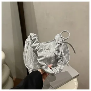 Macro view of silver ruched handbag featuring a metallic bow detail and pleated handle