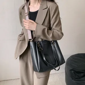 Bolso tote negro de cuero con correa vintage llevado por modelo con blazer marrón