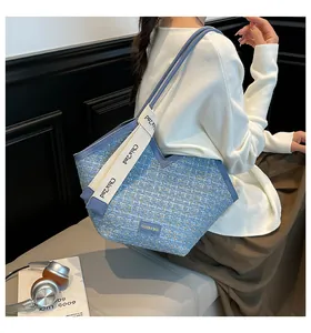 Close-up of a blue tweed tote bag with woven texture and branded white shoulder straps