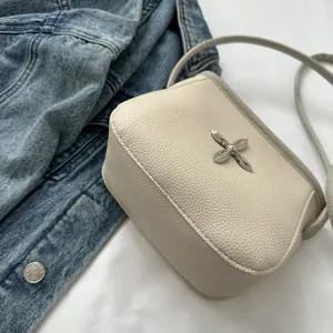 Détail du sac bandoulière en cuir grainé blanc cassé avec boucle métallique en croix