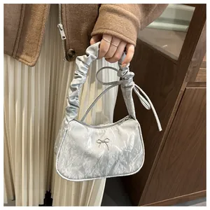Close-up of a silver pleated underarm bag with a metal bow and ruffled handle detail