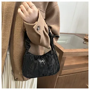 Detail of black pleated underarm bag featuring a metallic silver bow and zipper closure