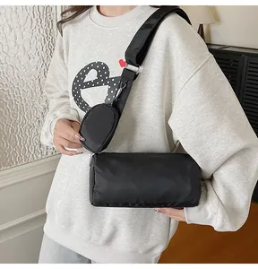 Detail of a black nylon cylinder crossbody bag with a round coin purse and wide strap