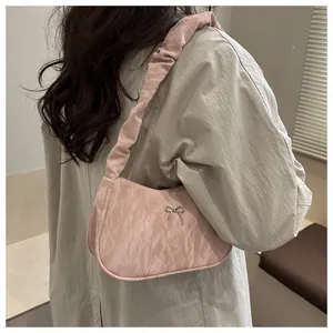 Detailed view of pale pink pleated underarm bag with a silver bow charm on the shoulder strap