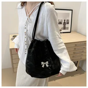 Detail of black pleated bucket bag with silver metal butterfly and thin straps on model