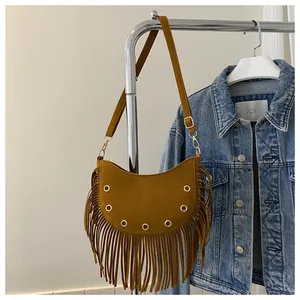 Detail of caramel suede half-moon bag featuring metallic eyelets and long fringe accents