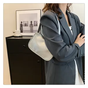 Modische silberne Schultertasche aus Leder mit Lychee-Muster auf einem schwarzen Schrank