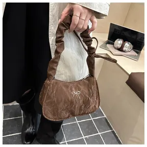 Detail of coffee brown pleated underarm bag with a silver bow decoration on a desk