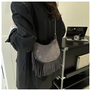 Detail of dark gray suede crossbody bag with metal eyelets and long decorative fringe
