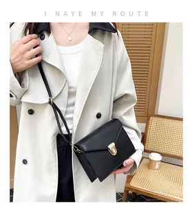 Minimalistische schwarze Umhängetasche aus Leder mit Goldschnalle auf hellem Trenchcoat