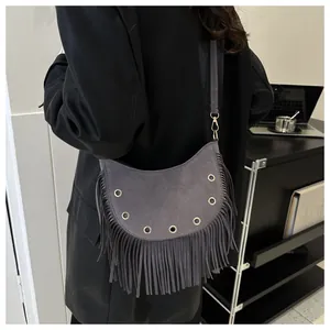 Macro view of grey crescent bag with tassels and metallic eyelets worn on shoulder