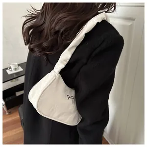 Detail of white pleated underarm bag with a small black bow decoration on a model
