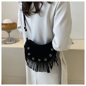 Detail of black crescent crossbody bag with golden grommets and fringe tassels on a model