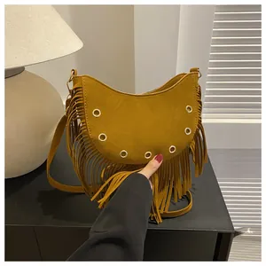 Detail of bohemian suede crossbody bag with long fringes and gold metal eyelets