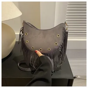 Detail of grey suede crescent bag featuring long tassels and gold metal eyelets decoration