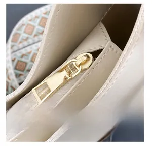 Dettaglio della cerniera dorata su borsa in pelle beige con tracolla tessuta