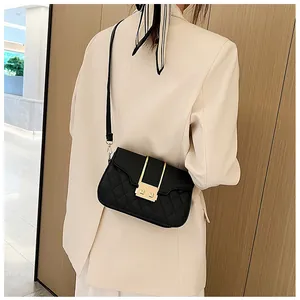 Detail of black quilted crossbody bag with golden U-shaped hardware on white blazer