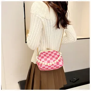 Detail of pink checkerboard crossbody bag with pearl handle and metal chain on a model