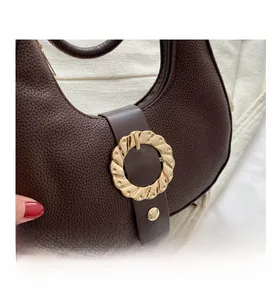 Close-up of deep brown lychee grain leather with a golden wave-textured buckle on the bag