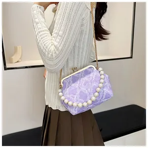 Detail of light purple kiss-lock bag with pearl handle and golden chain on model