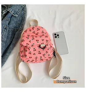 Mini pink corduroy cherry backpack size comparison next to a modern smartphone