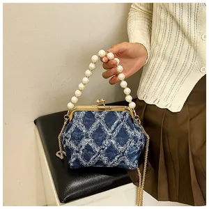 Detail of blue denim quilted bag featuring faux pearl handle and gold kiss-lock clasp