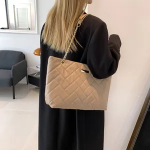 Quilted beige tote bag with gold chain strap shown on model in a modern interior