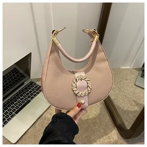 Detail of lychee textured beige crescent bag featuring a large golden wavy ring buckle