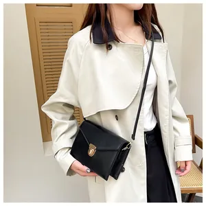 Modische schwarze Umhängetasche mit goldener Schnalle zu einem beigen Trenchcoat