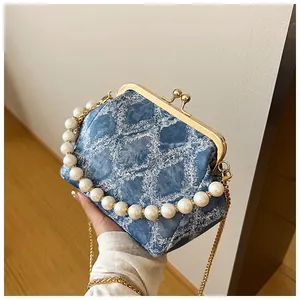 Detailopname van blauwe denim handtas met parelhandvat en gouden kettingbandje
