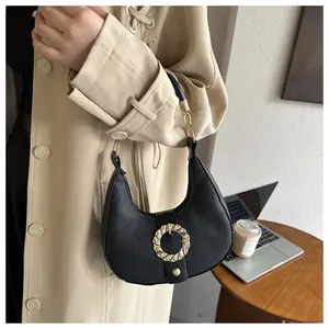 Detail of black pebbled leather crescent bag featuring a prominent gold spiral buckle